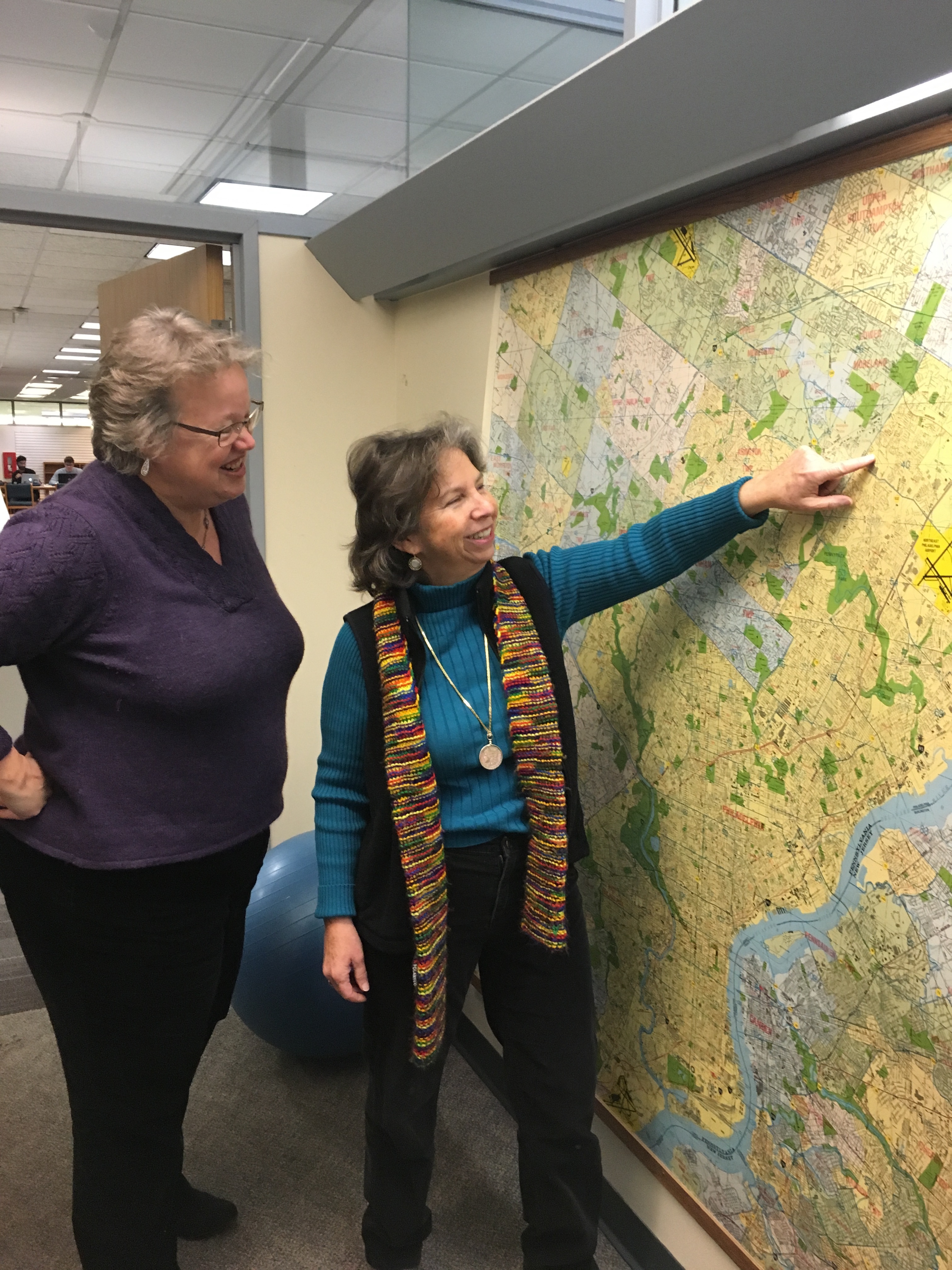 Two women examine a map of Philadelphia that is mounted to the wall in an office.