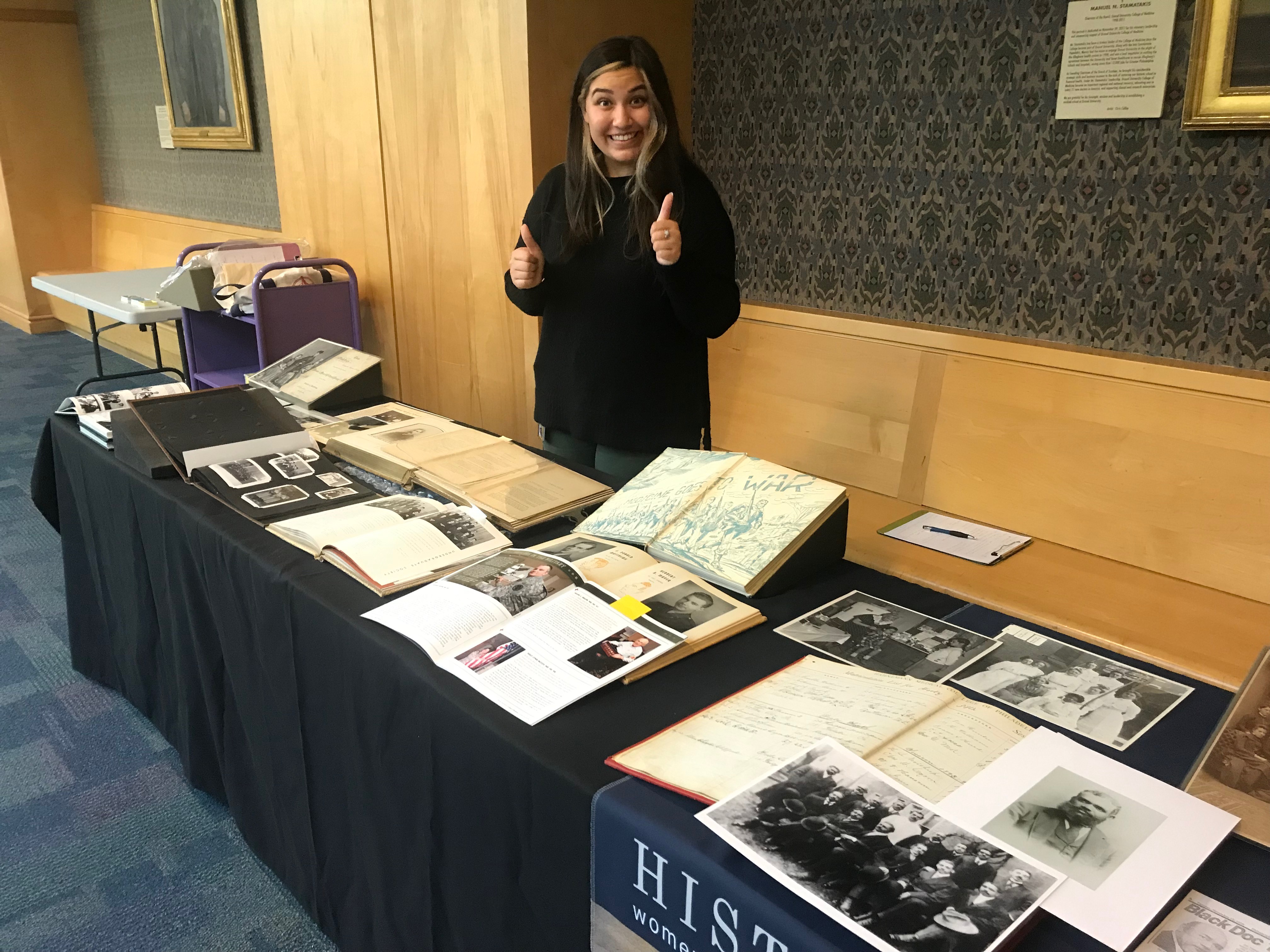 A woman stands next to a table lined with books and documents