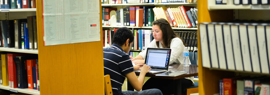 Two students working on a project together in the library stacks.