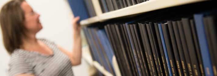 A librarian going through a collection of bound theses.